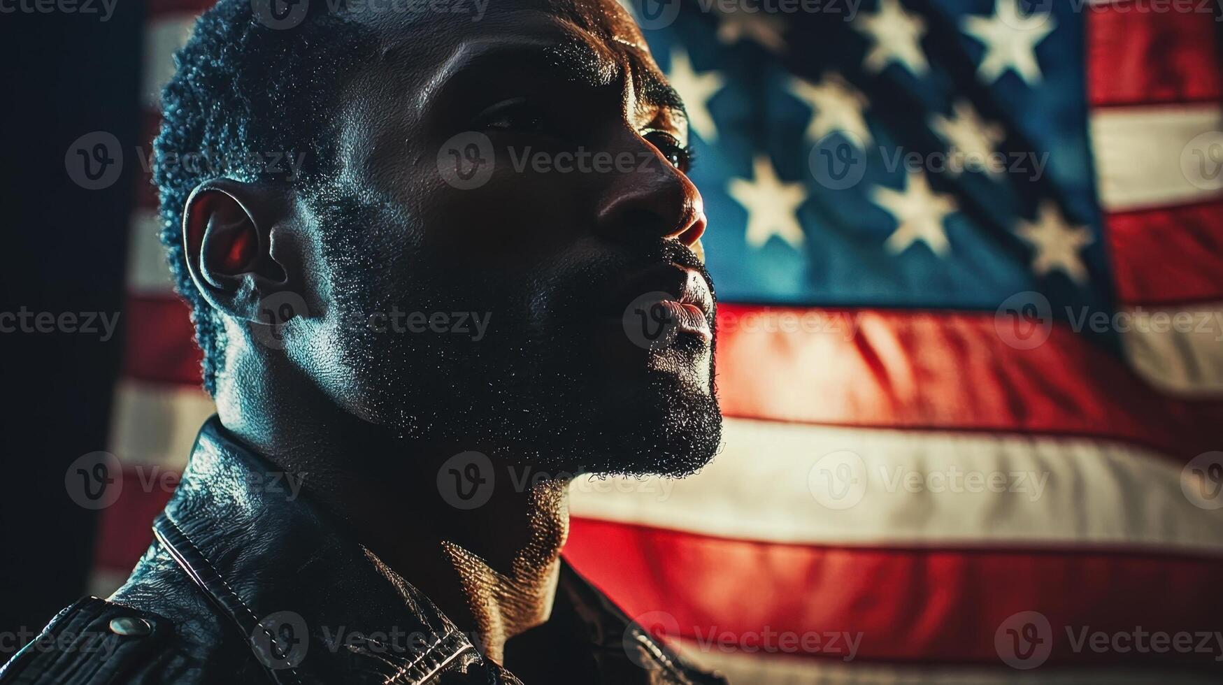 A confident man stands in profile with a serious expression in front of a large American flag. The warm lighting highlights his features, evoking a sense of pride and resilience photo