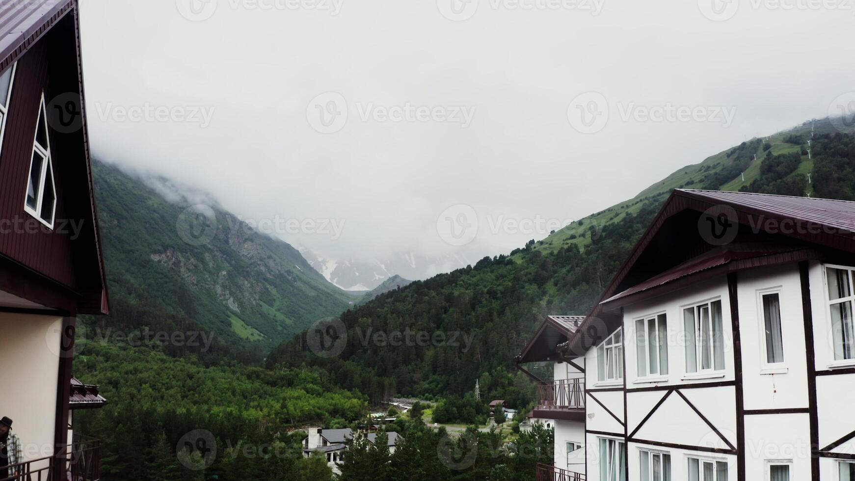 Tourist complex in mountains. The building of hotel at the foot of the rocky mountains, the peaks of which are covered with snow and clouds, filmed from a drone. Mountain nature of the Caucasus photo