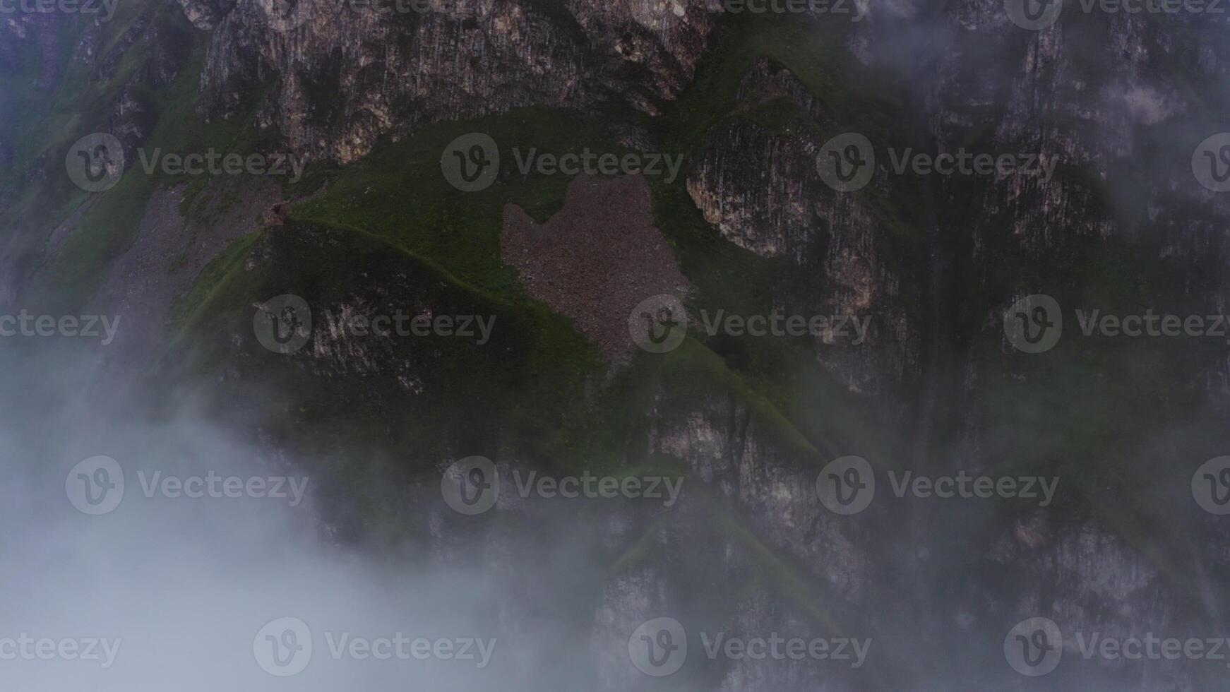 Shooting from a quadcopter, top view through the clouds on the steep rocky mountains covered with green vegetation photo