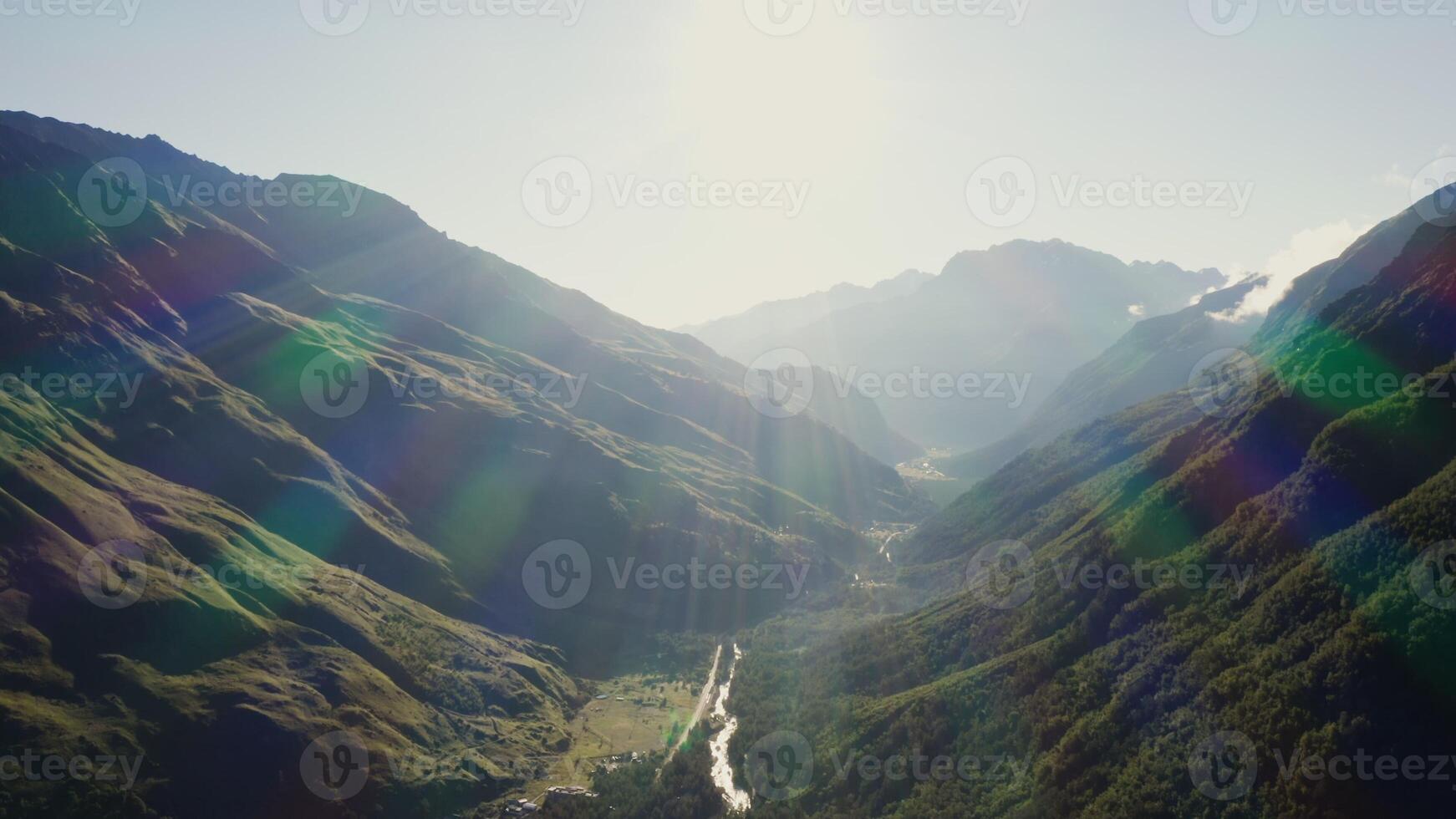 Panoramic shot from a bird's eye view, a view of the mountain valley in the rays of the rising sun. A mountain settlement with a river in the lowland is flooded with sunlight. photo