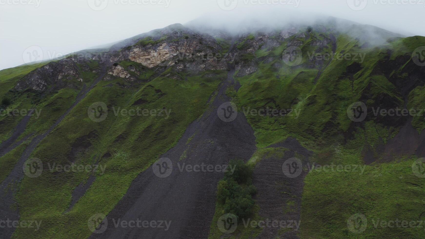 Shooting from a quadcopter, a view of the steep rocky mountains covered with green vegetation. The peaks of the mountains are covered with thick clouds photo