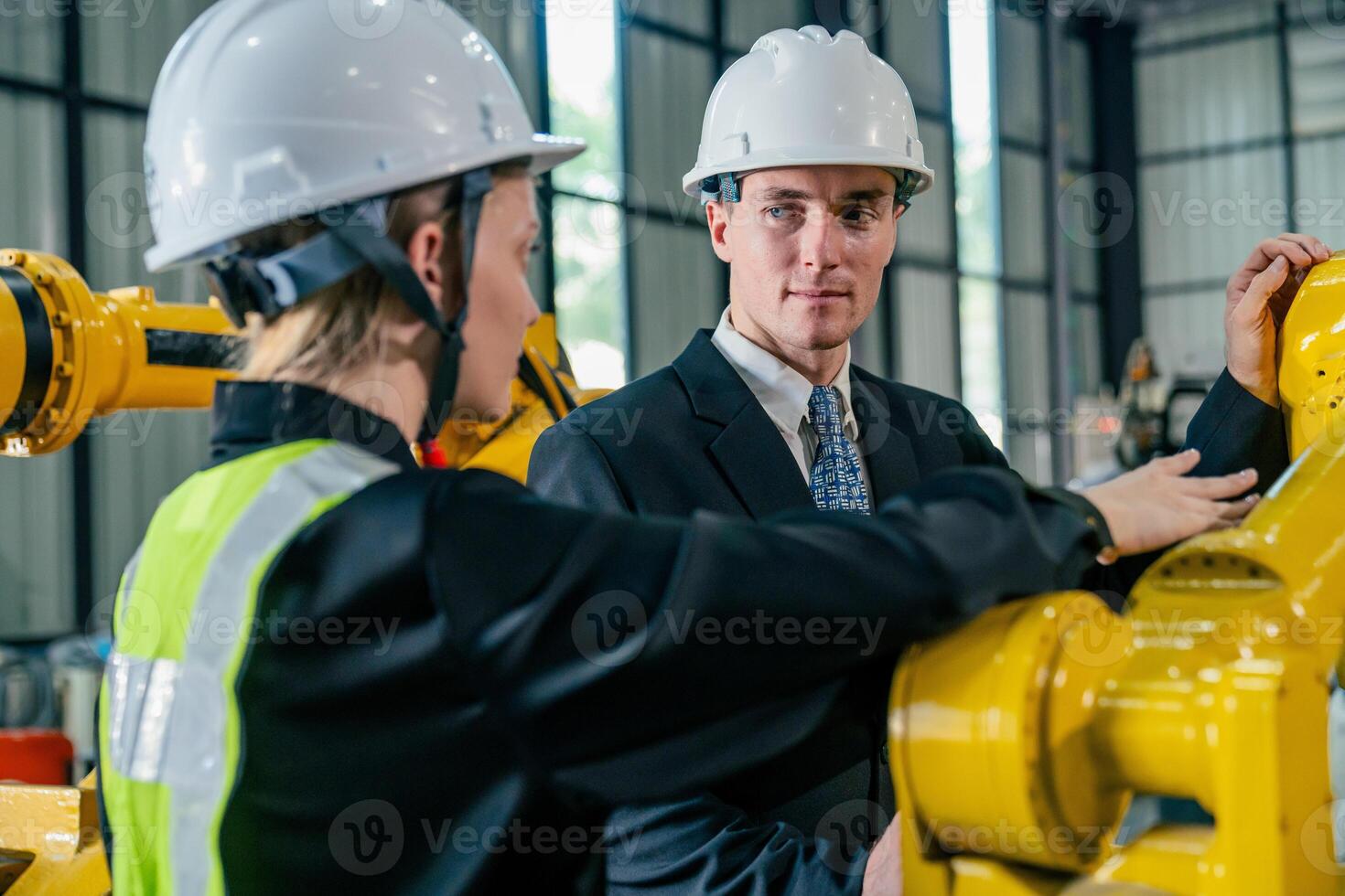Professionals in safety helmets discuss industrial machinery in a factory setting during daylight hours photo