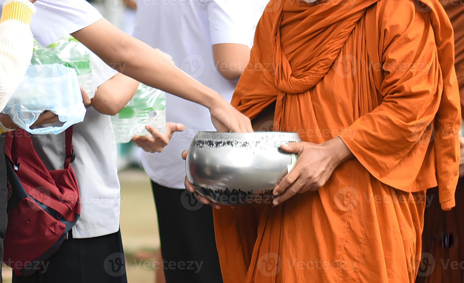 A monk is holding a silver bowl and giving it to a person photo