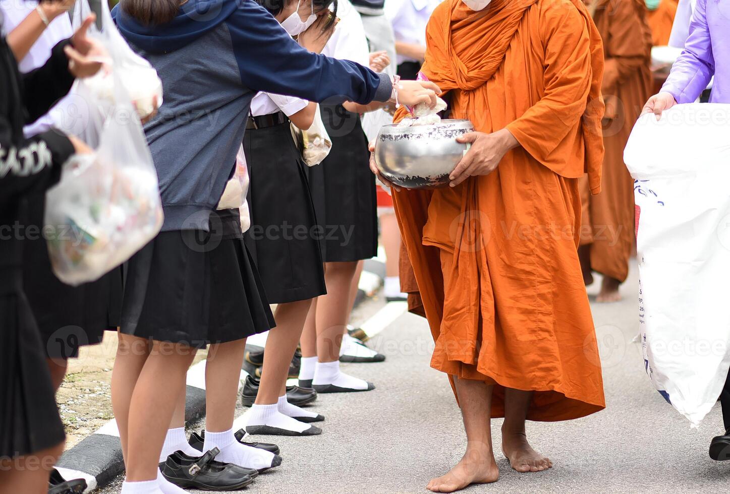 A man in an orange robe is handing out food to a group of people photo