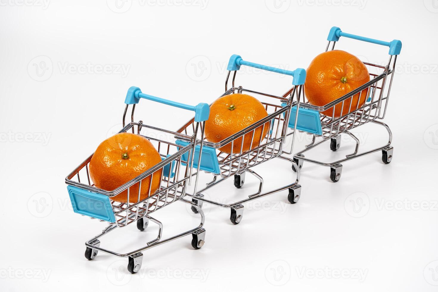Three miniature shopping carts with oranges lined up on a white surface photo