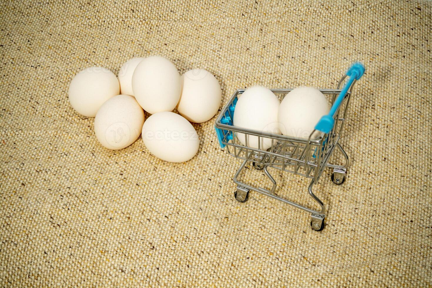 Small shopping cart with eggs next to a larger pile on fabric photo