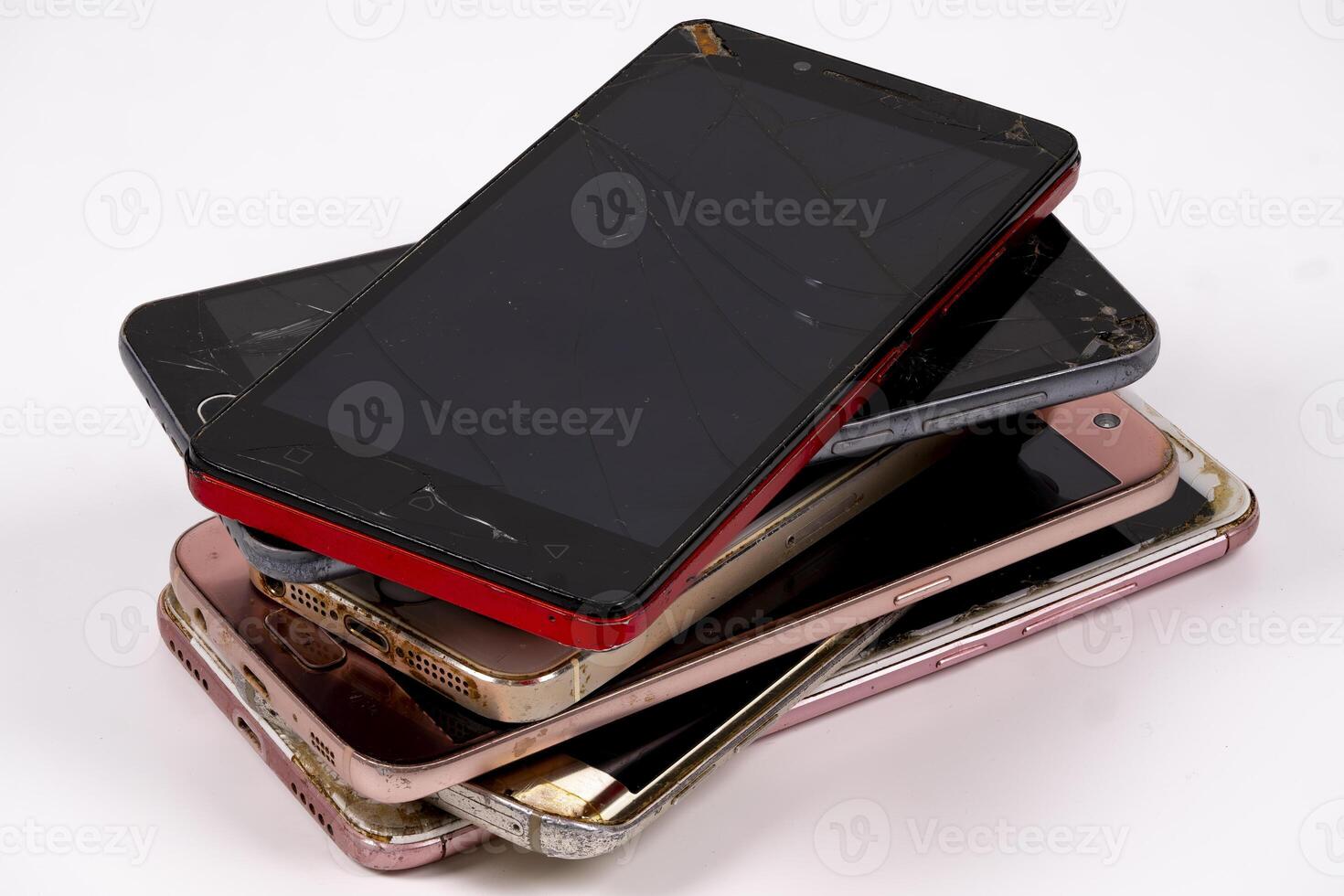 Old and broken smartphones stacked in a messy pile on a table photo