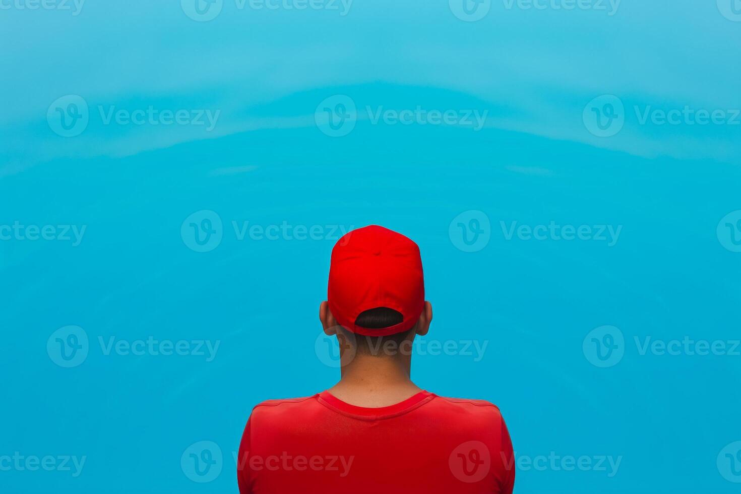 Lifeguard in a red cap stands at the edge of a calm blue waterpool, ready for duty photo