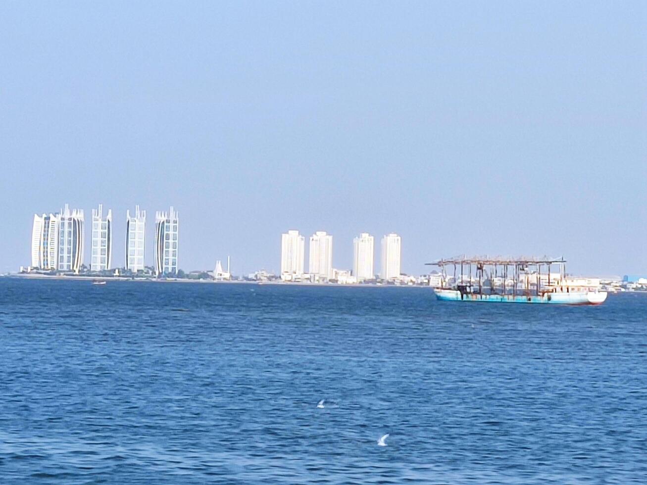 a view of the sea on a clear day, there are tall buildings and fishing boats passing by on the sea. photo