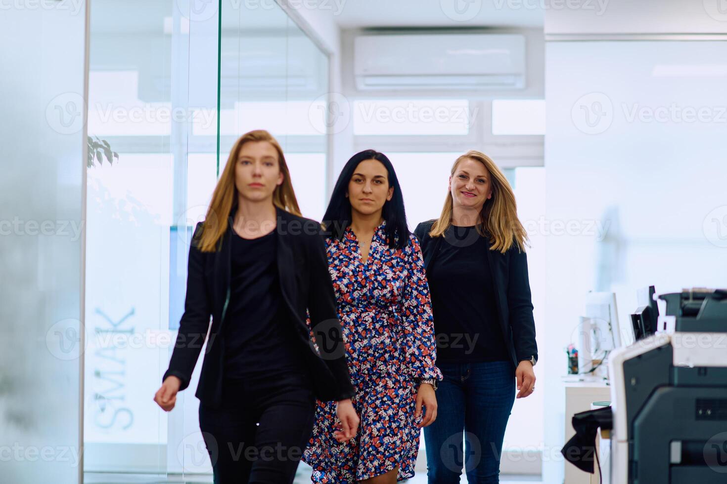 Confident businesswomen stride through the office hallway, deep in discussion. photo