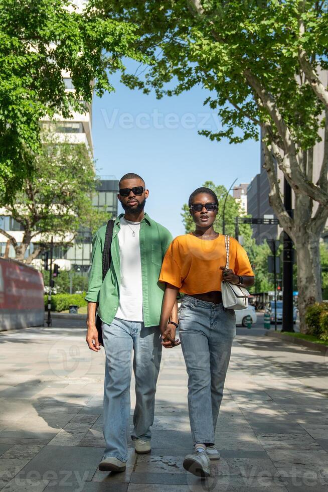 Serious boyfriend, cheerful girlfriend on date. Black couple holding hands wander, walk around town. photo