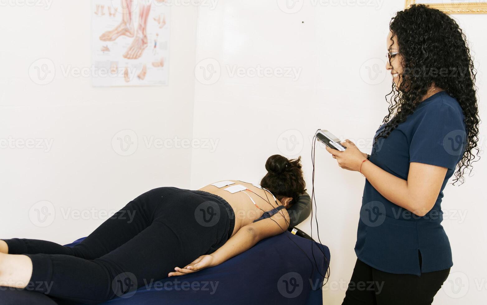 Physiotherapist electrostimulating a patient. Lower back therapy with electrode pads. Electrode treatment to patient lying down, Professional physiotherapist electrostimulating a lying patient photo