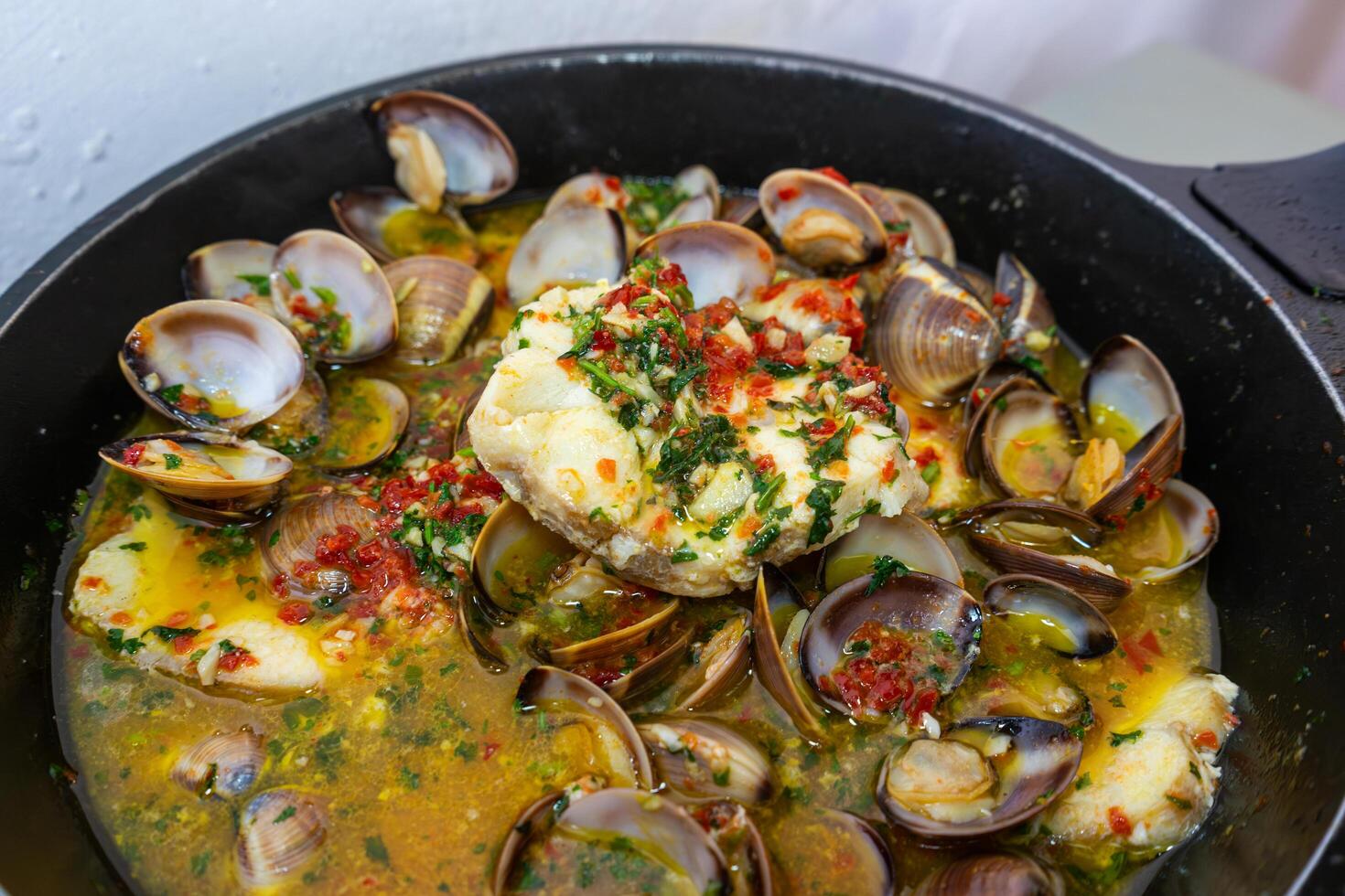 Delicious Alentejo-style dogfish with clams, featuring tender fish and savory clams in a rich, flavorful sauce, served with fresh herbs and a sprinkle of paprika. photo