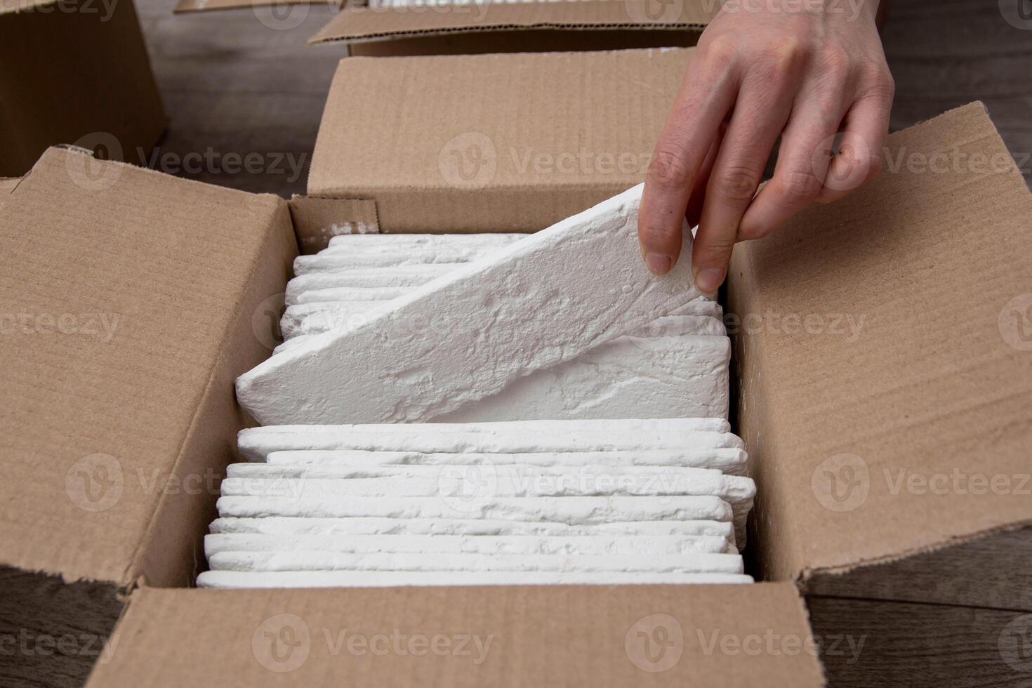A man's hand takes out a white decorative stone from a box. Decorative stone in the form of a brick, close-up photo
