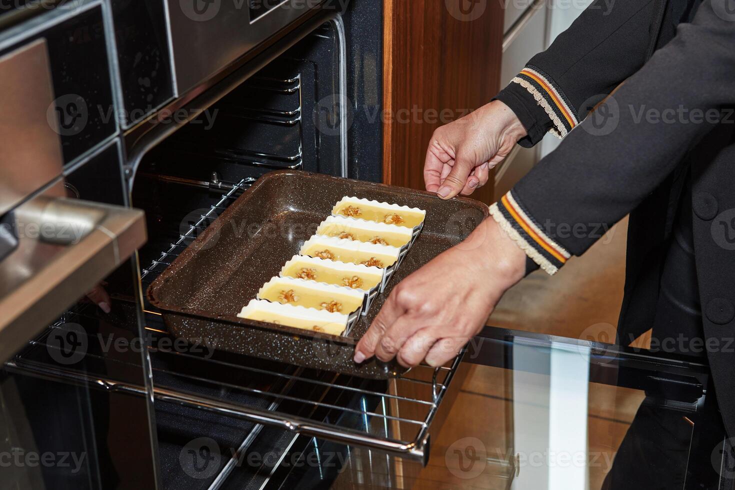 A person places a baking tray filled with walnut-topped muffin batter into the oven, starting the baking process in a cozy kitchen. photo