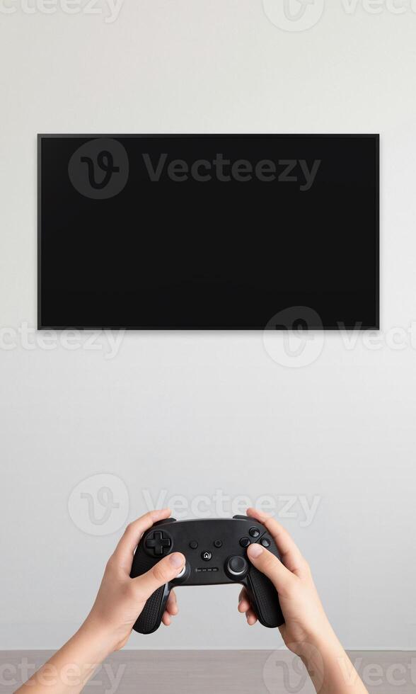 Blank TV mounted on a wall with a gamepad in hands, vertical composition, ideal for promoting games and immersive home entertainment setup photo
