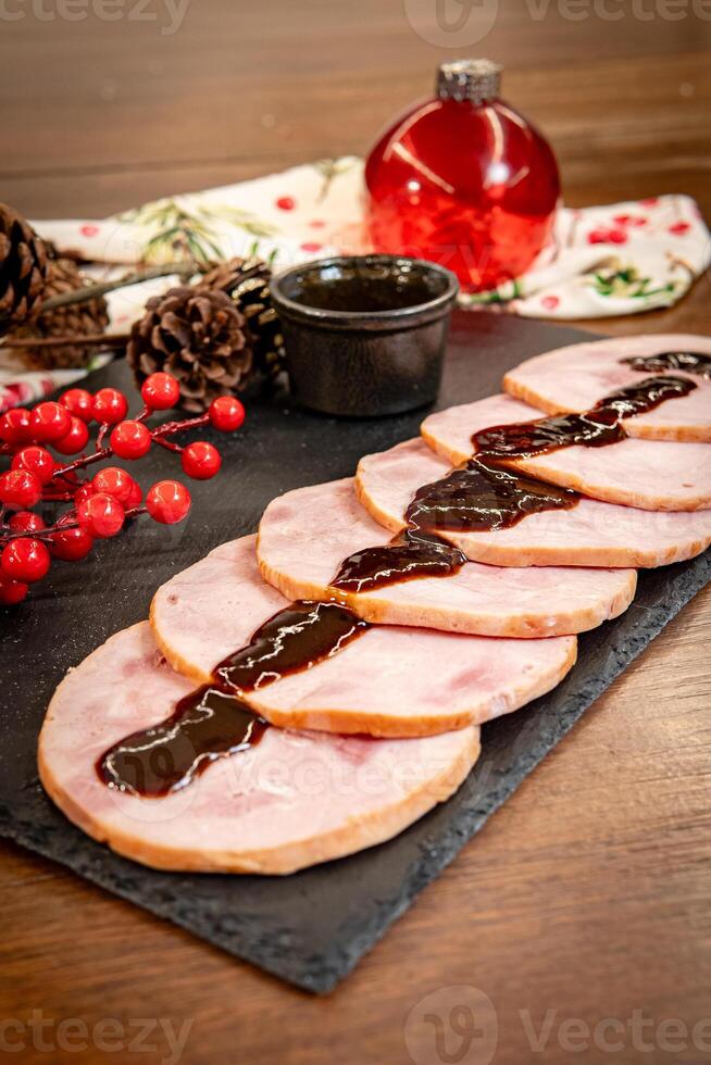 Slices of Christmas pork leg pernil with plum sauce and festive decorations on a wooden board. photo