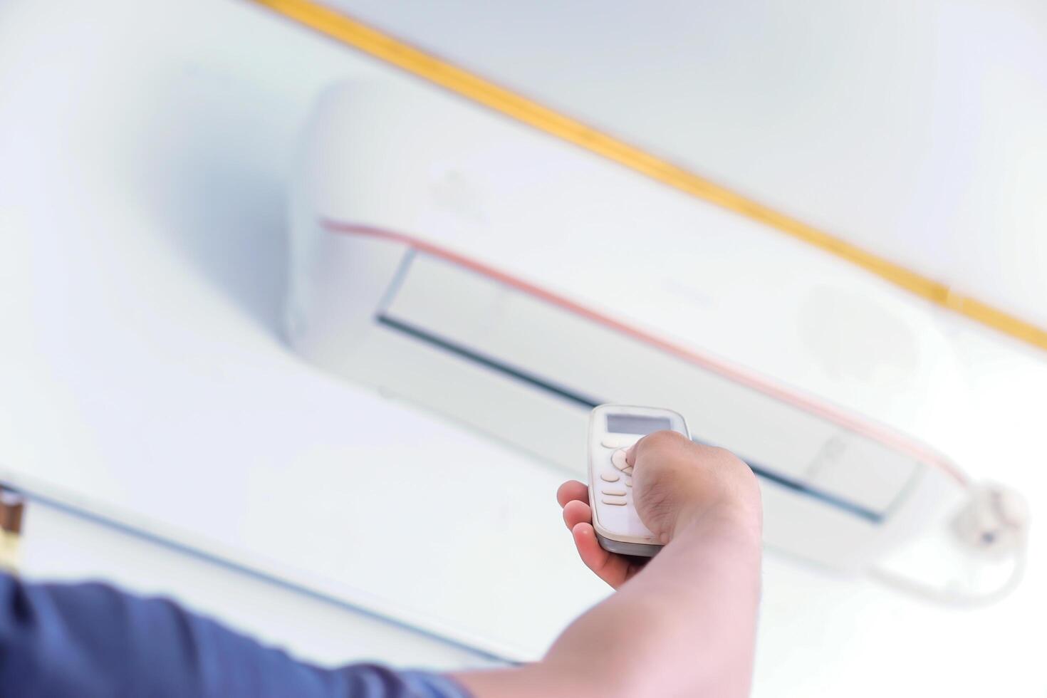 A person using a remote control to adjust an air conditioning unit mounted on the wall. photo