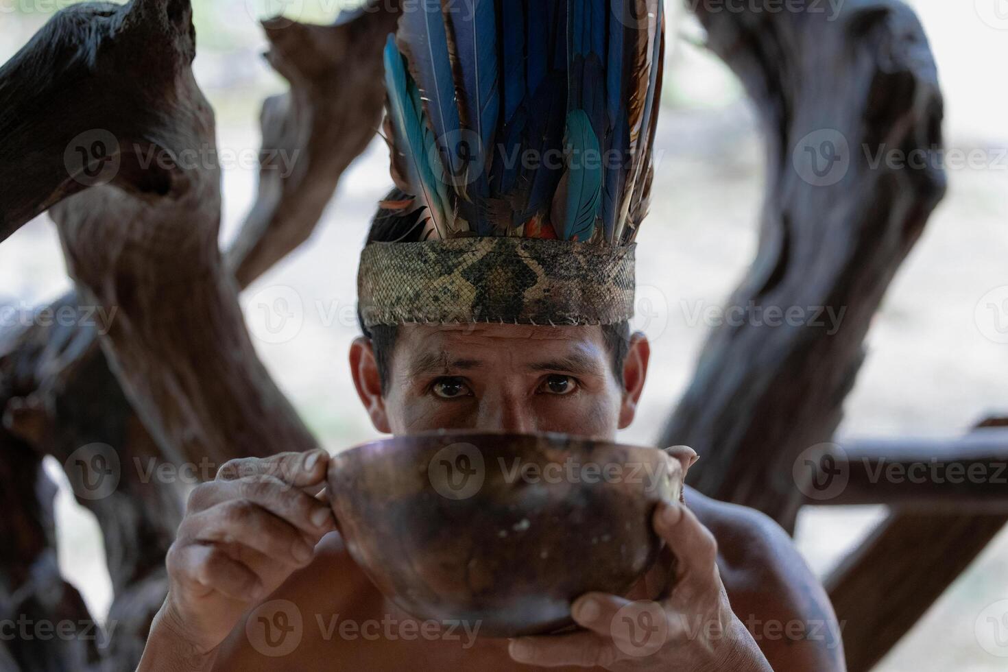 Indigenous Wayuri Man Drinking Chicha from Bowl Wearing Feather Crown in Puyo, Ecuador photo