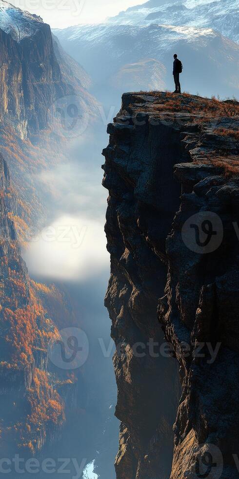A man stands on the edge of a cliff overlooking a valley photo