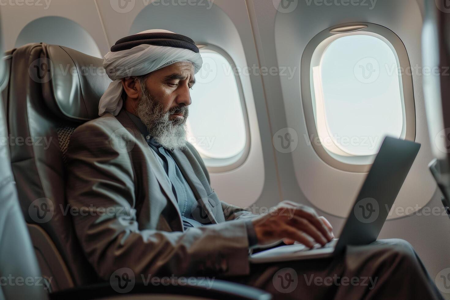 An arab man sitting on an airplane using a laptop photo