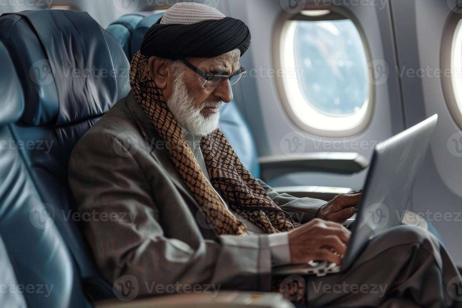 An old man sitting on an airplane using a laptop photo