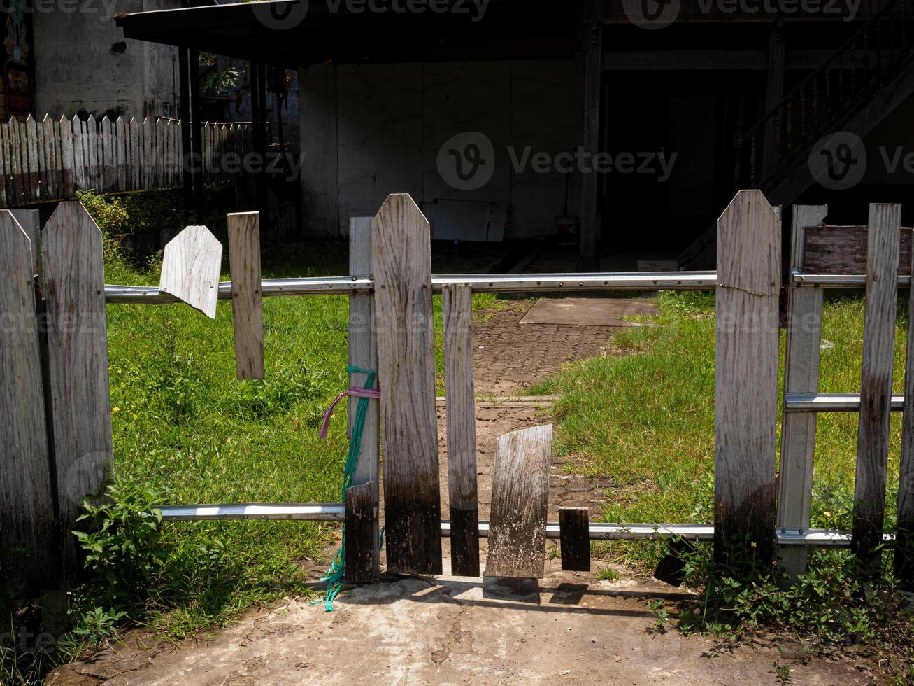 A horizontal shot of rundown white picket fence reinforced with steel and wire showing wide holes photo