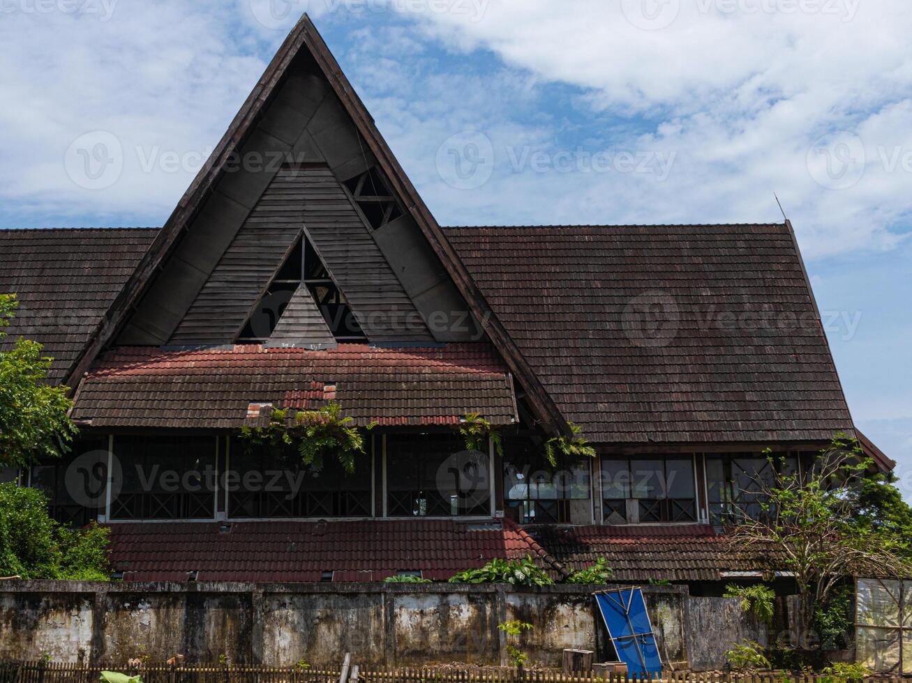 An abandoned two stories convention hall with traditional architecture with overgrown fern and broken windows and tiles shot from low angle in a sunny day photo