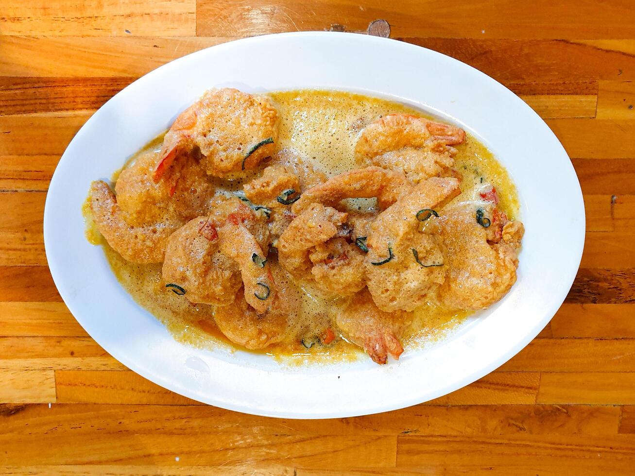 Simple flatlay shot of Fried shrimp with salted egg sauce served on white ceramic plate with jointed wood background photo