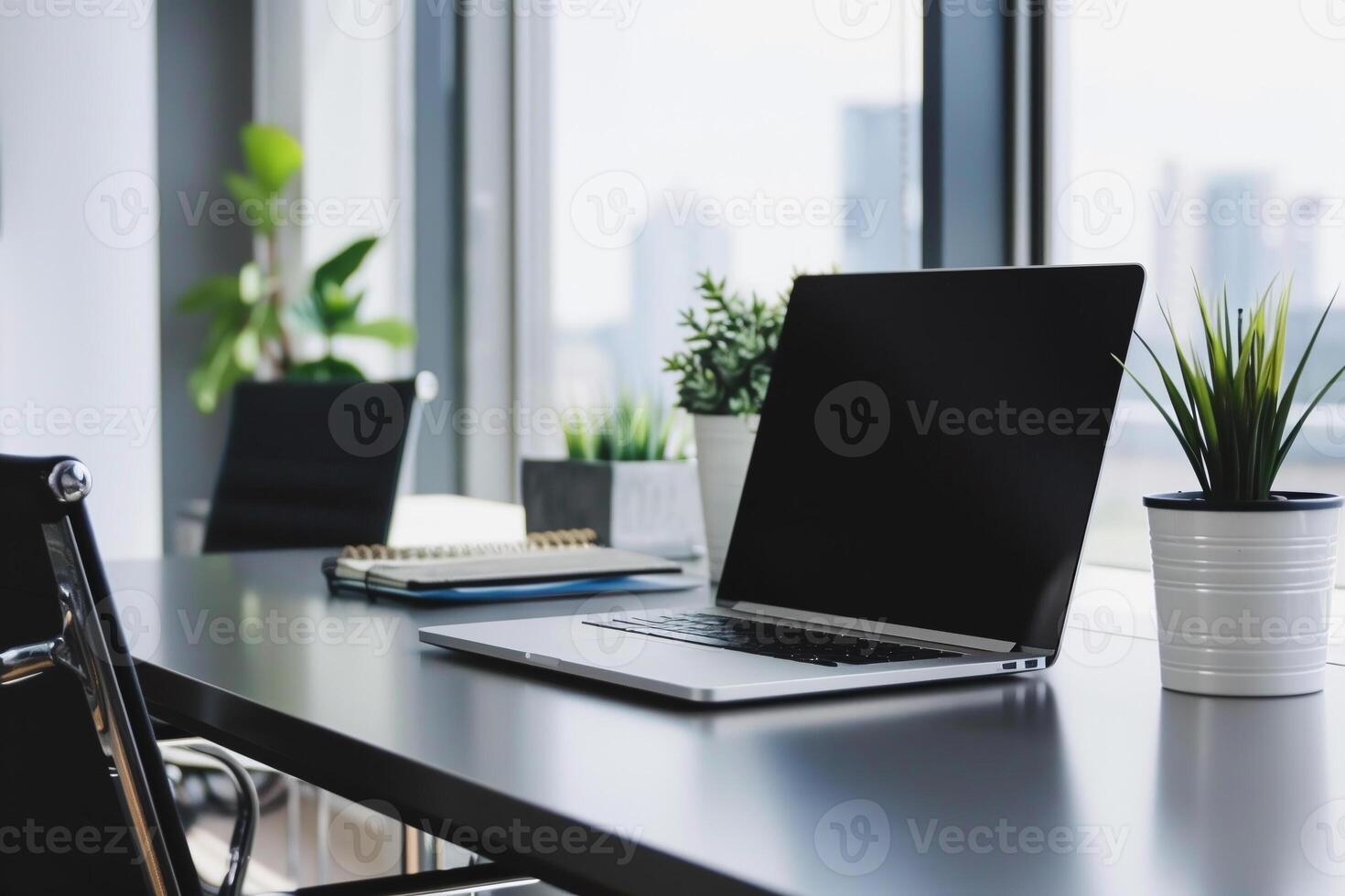 A laptop is on a desk with a potted plant and a notebook photo
