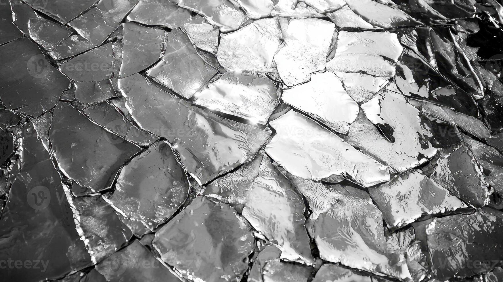 Textured surface displays an intricate pattern of cracks, reflecting light in various shades of gray. The interplay of light and shadow creates a visually striking monochrome effect photo