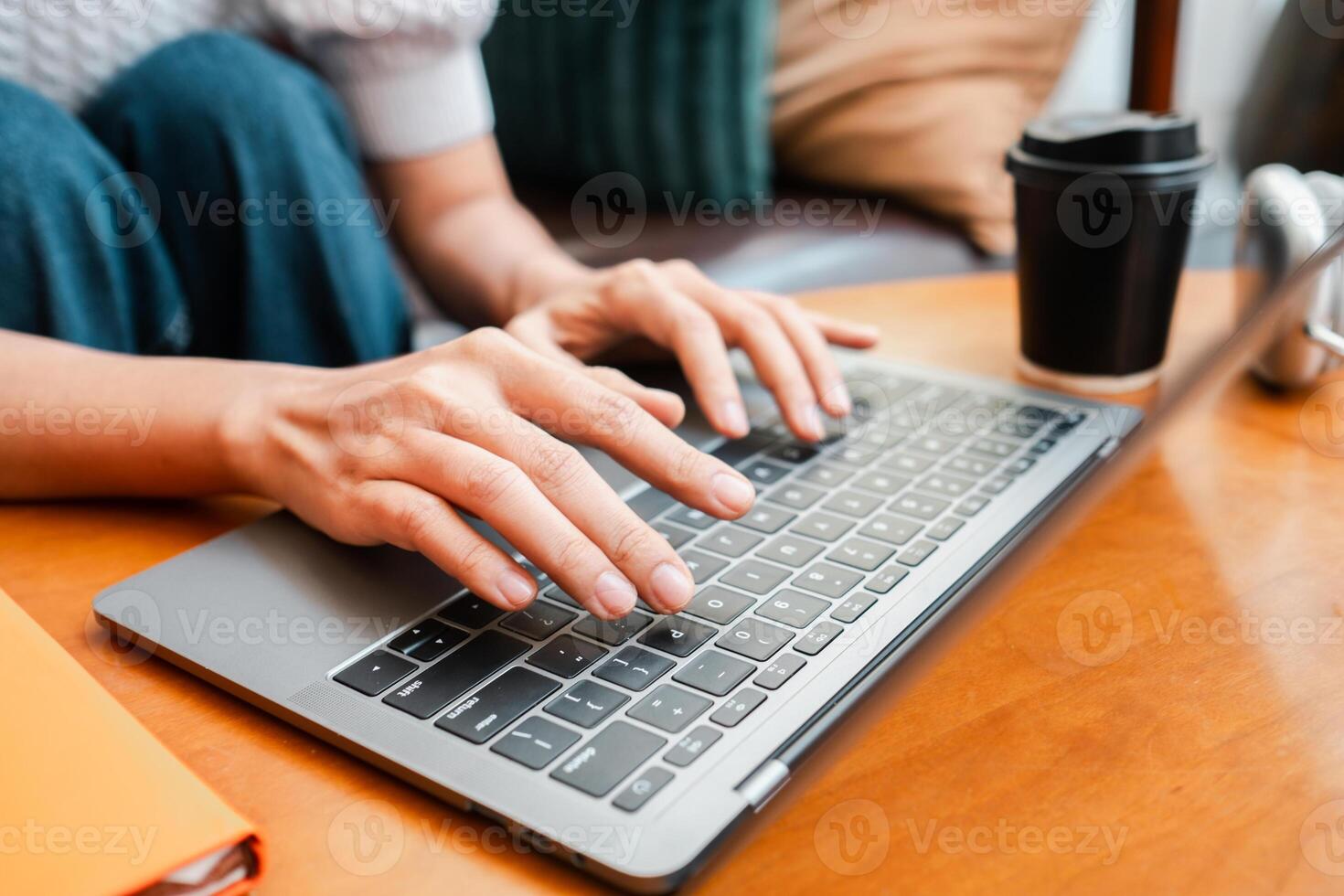 Hands typing on a laptop keyboard with a coffee cup nearby, set on a wooden table in a cozy indoor environment. photo