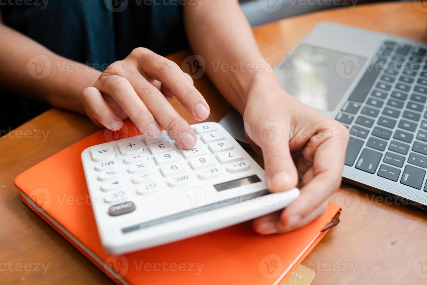 Close-up of hands using a calculator on a desk with a laptop and notebook, ideal for financial planning and budgeting concepts. photo