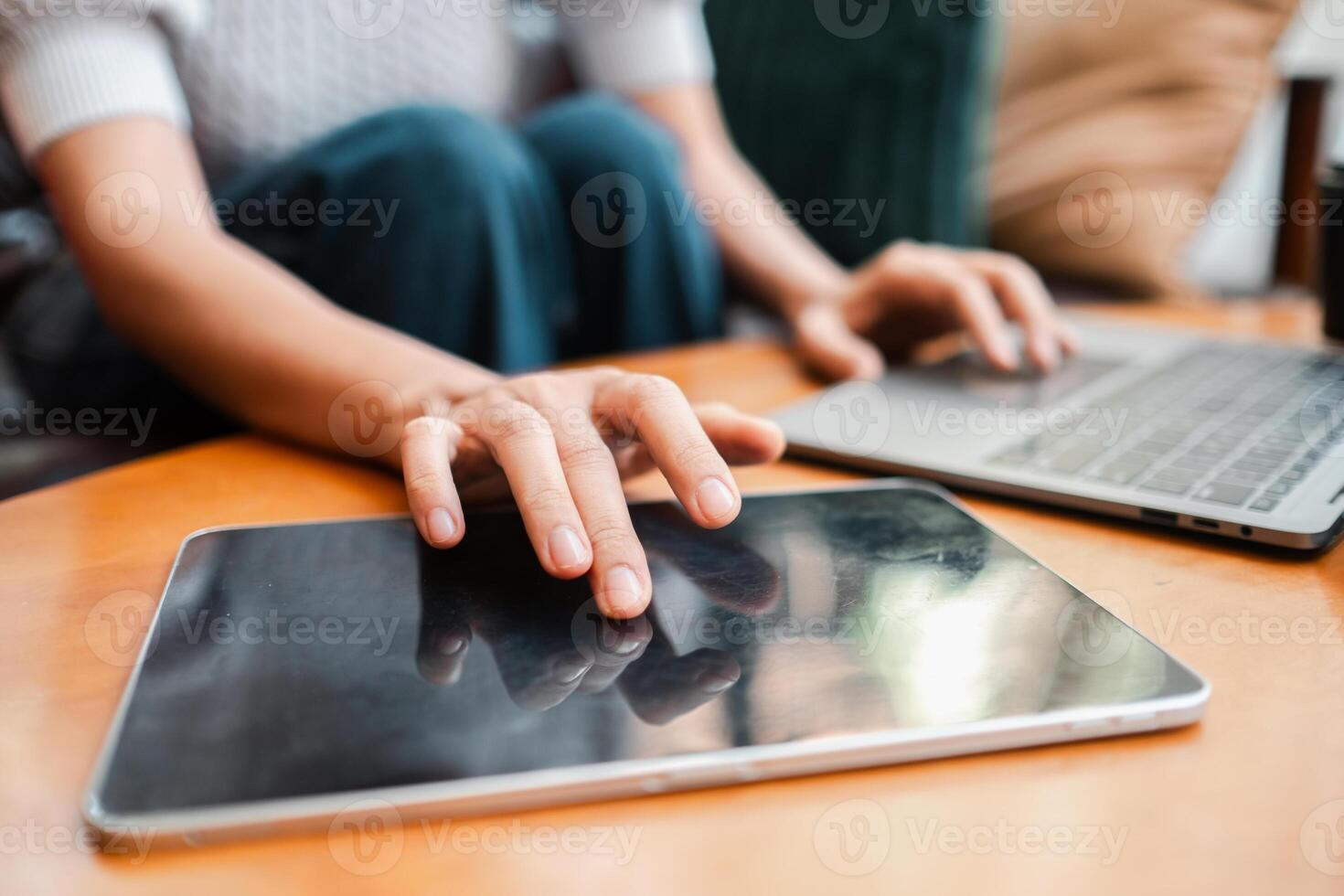 Hands interacting with a tablet and laptop on a wooden table, showcasing modern technology use in a home setting. photo