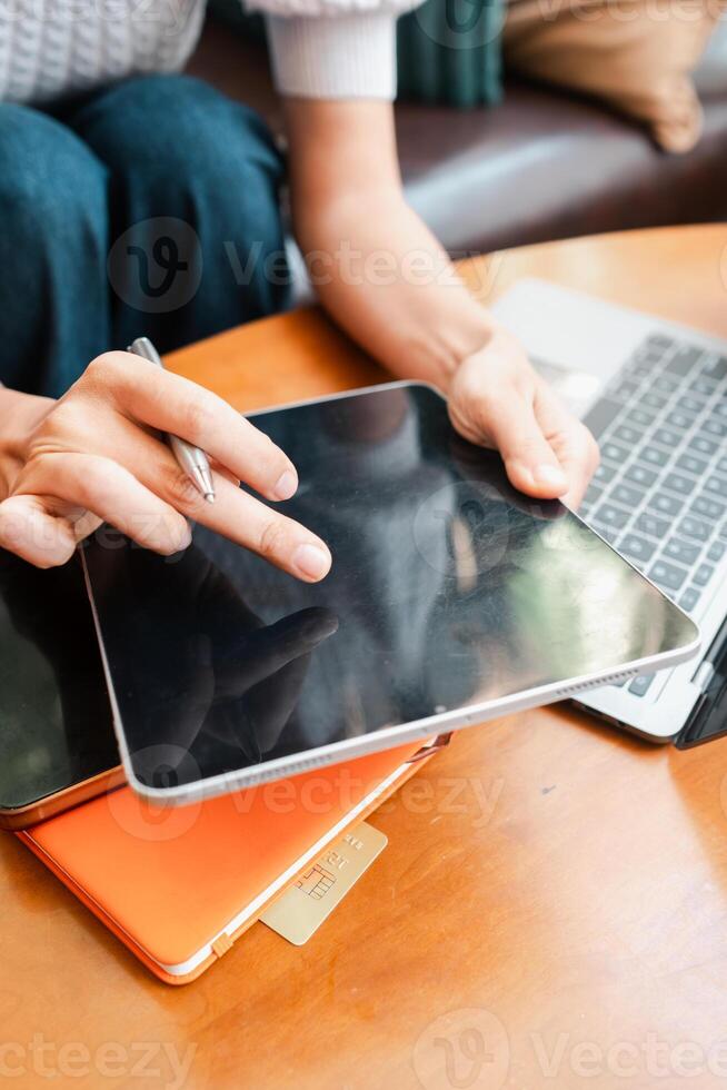 Close-up of hands using a digital tablet with a stylus, next to a laptop, on a wooden table in a casual environment. photo