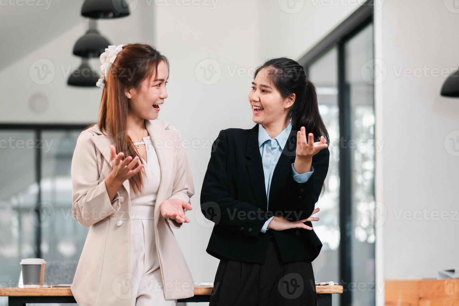 Two businesswomen in a modern office, smiling and talking, showcasing teamwork and communication. photo