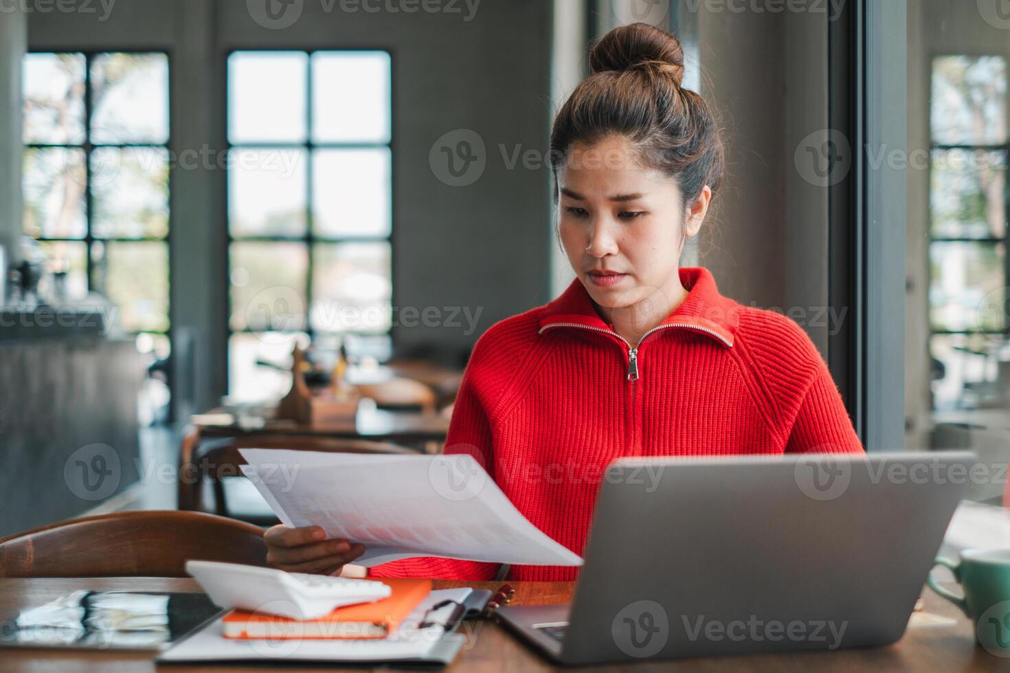 Woman in a red sweater working on a laptop in a modern cafe, reviewing documents with concentration. photo