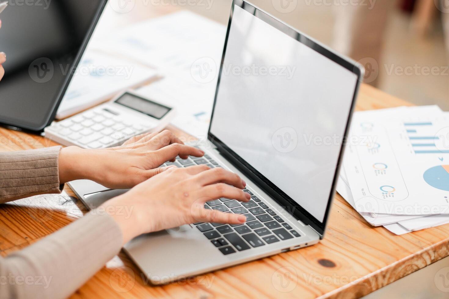 Hands typing on a laptop with financial documents and a calculator on a wooden desk, depicting a modern office environment. photo