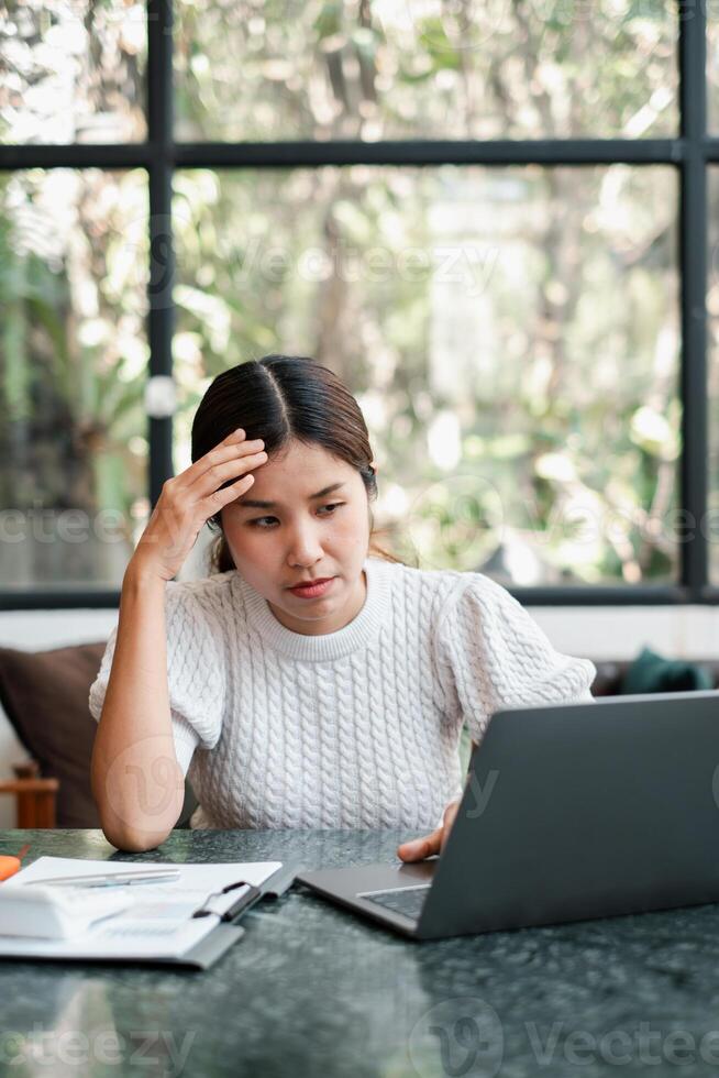 Focused woman working on a laptop in a modern office with large windows and greenery outside. photo