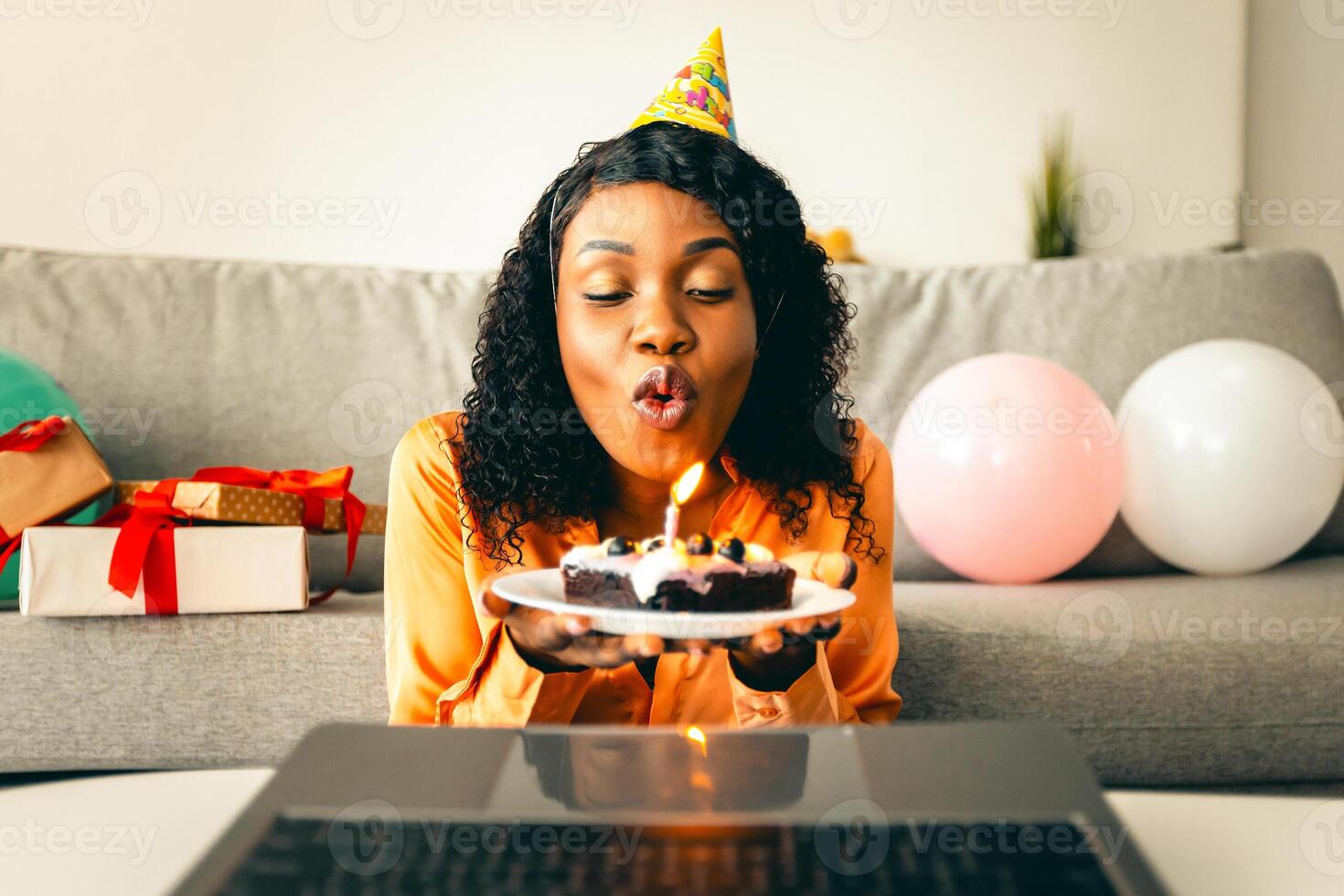 Happy Birthday. Black Lady Blowing Candle On Cake In Front Of Laptop Computer Celebrating Her Holiday Remotely, Having Virtual Party Via Call At Home. Modern B-Day Celebration photo