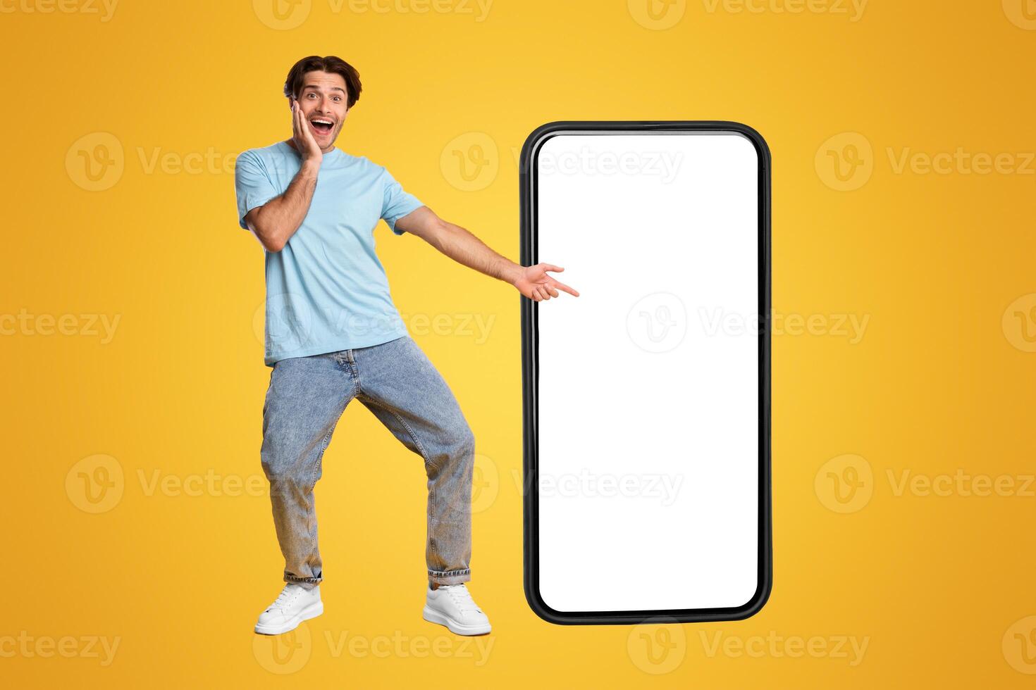 Great Mobile Offer. Excited Guy Pointing Finger At Big White Smart Phone Screen, Emotionally Reacting To New App, Overjoyed Young Male Standing Isolated Over Orange Studio Background, Mock Up photo