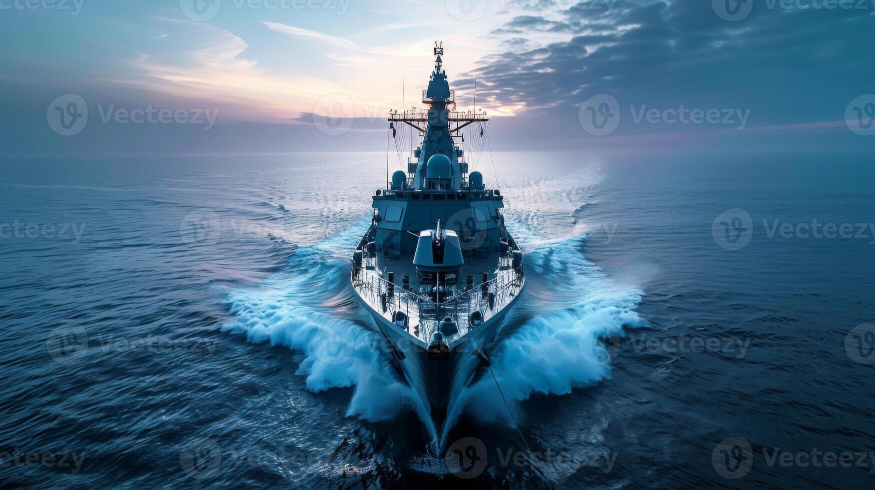 A powerful naval vessel glides smoothly through tranquil waters during sunset, creating waves that shimmer under the vivid colors of the evening sky. photo