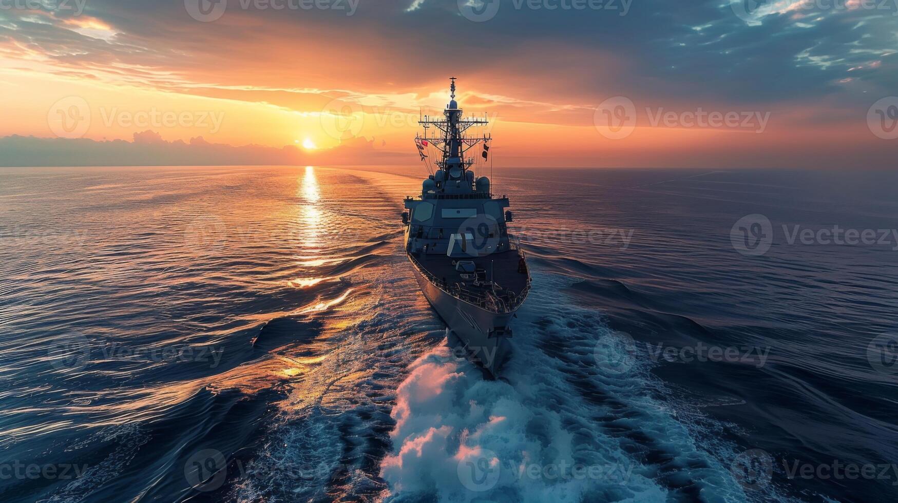A military vessel moves gracefully across the ocean as the sun sets on the horizon, illuminating the sky with shades of orange and purple while creating a trail in the water. photo