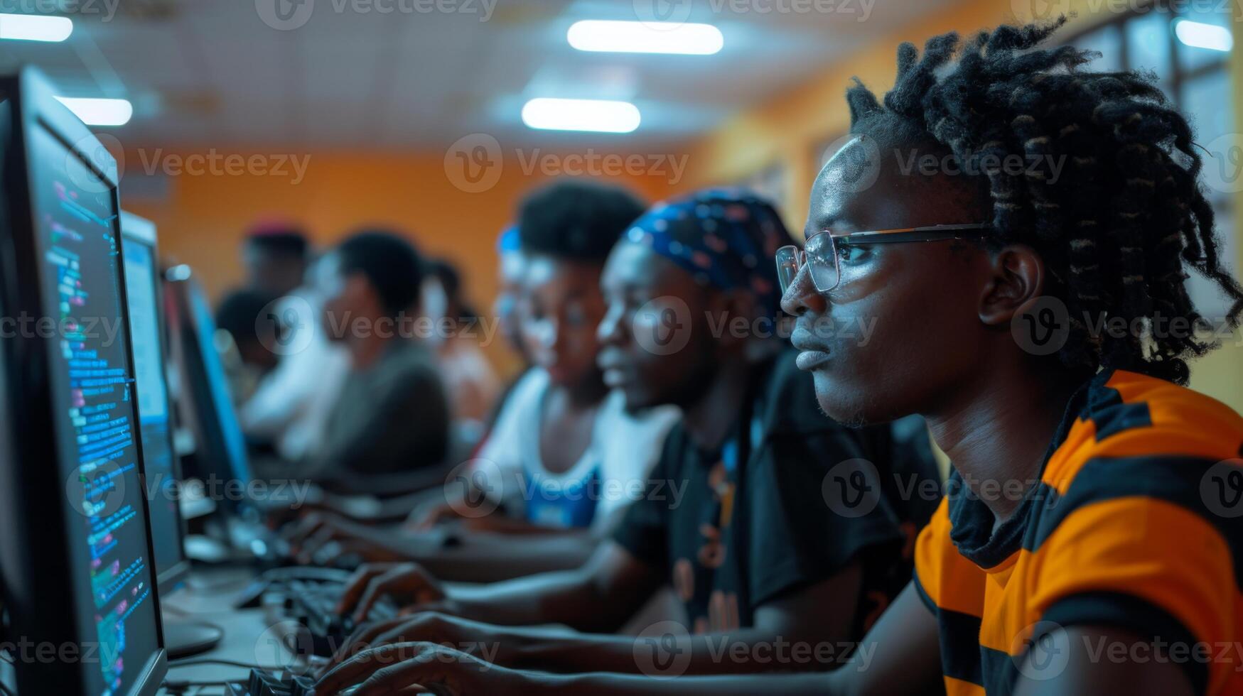 Young adults focus intently on their screens while coding in a lively computer lab setting, showcasing collaboration and learning in the evening light. photo