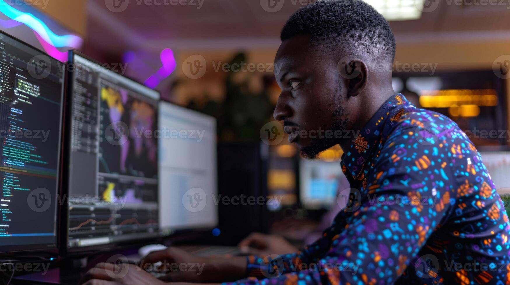 A young man intensely engages with multiple computer screens, analyzing data and writing code in a vibrant office environment during the evening. photo