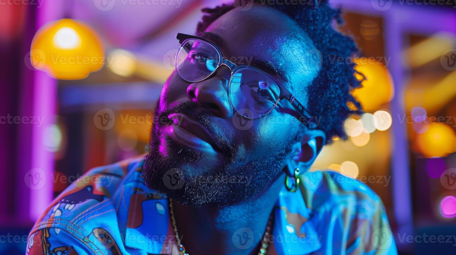 A stylish young man wearing round glasses and a colorful shirt is smiling at the camera in a lively cafe, surrounded by warm, ambient lighting and vibrant decor in the evening. photo