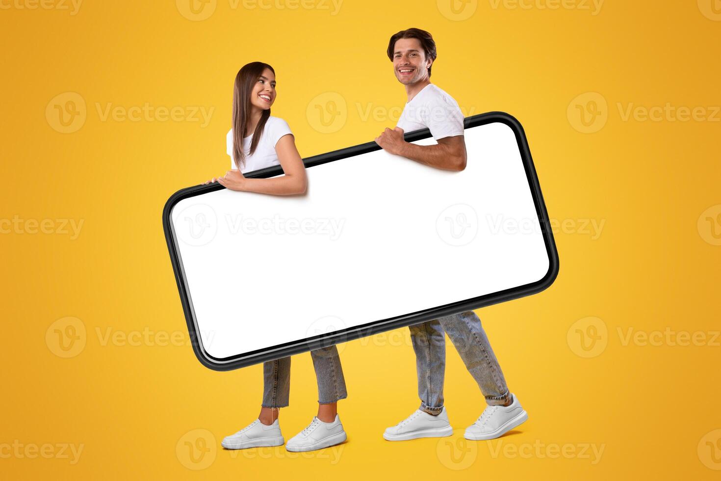 Cool Mobile App. Cheerful young couple holding big giant smartphone with mockup, walking together, promoting application or website, advertising your service or product over orange studio background photo