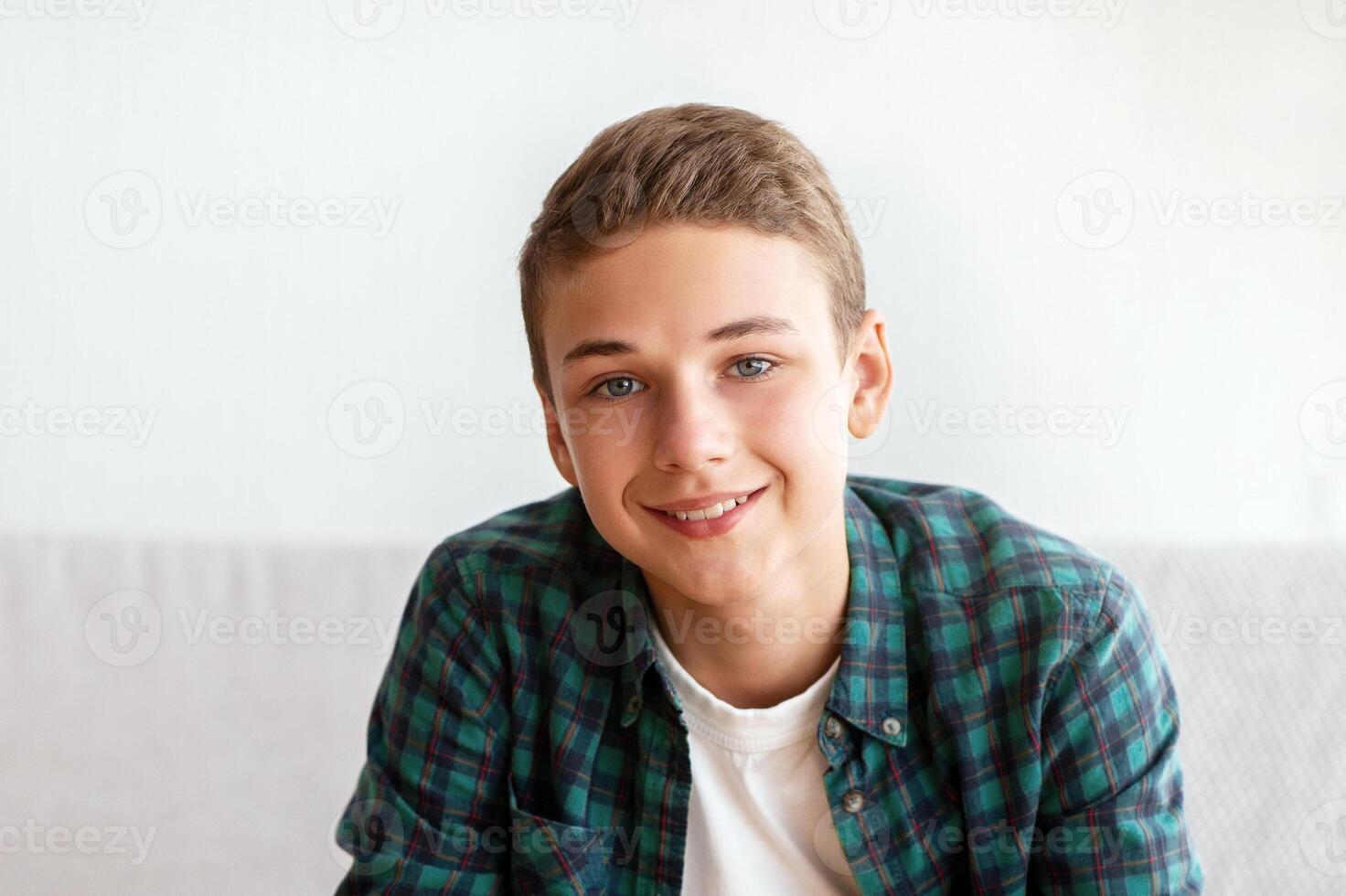 Cheerful teenager guy sitting on sofa at home, talking on camera, shooting for his followers, free space photo