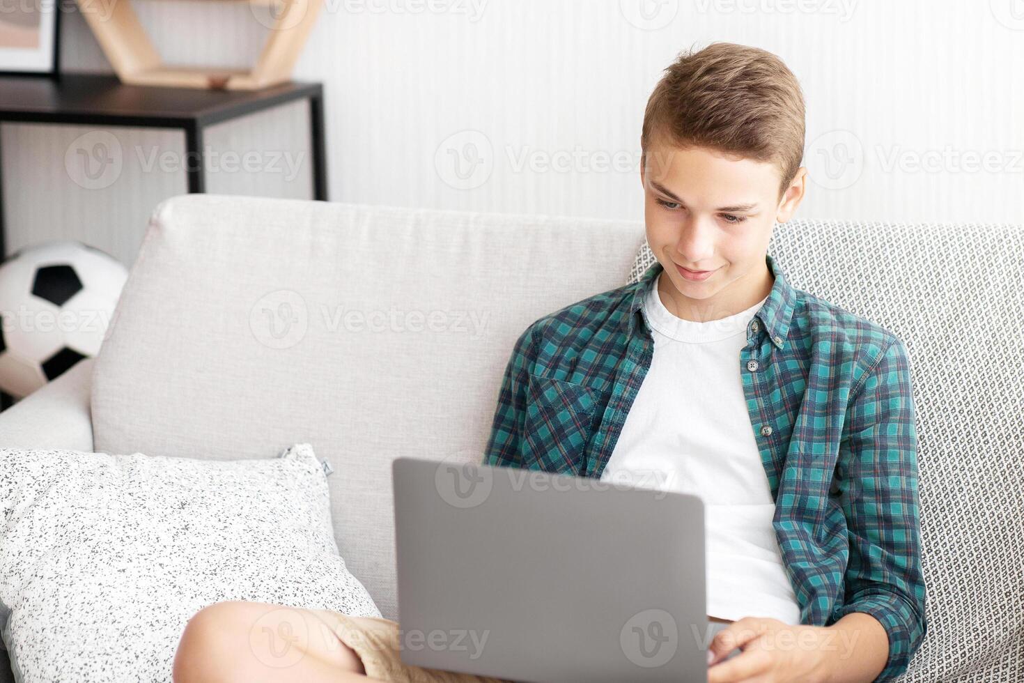Teenager with laptop sitting on sofa at his room, websurfing, copy space photo