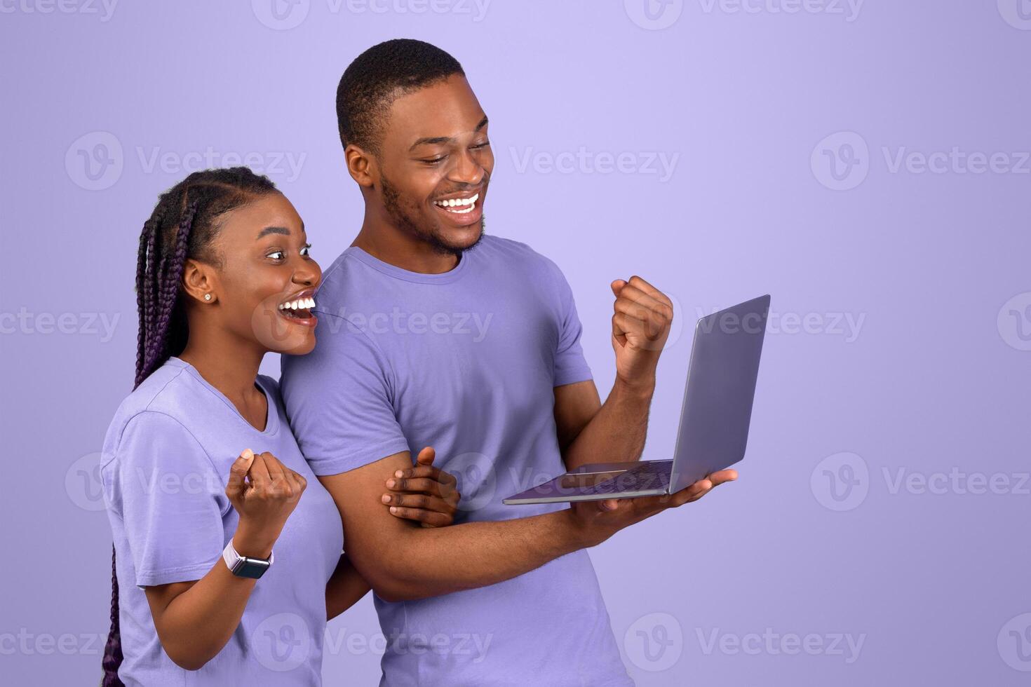 Yes, Big Win Concept. Excited young black couple holding using pc, cheering raising hands celebrating victory. Emotional happy guy and lady shaking clenched fists looking at screen, purple violet wall photo